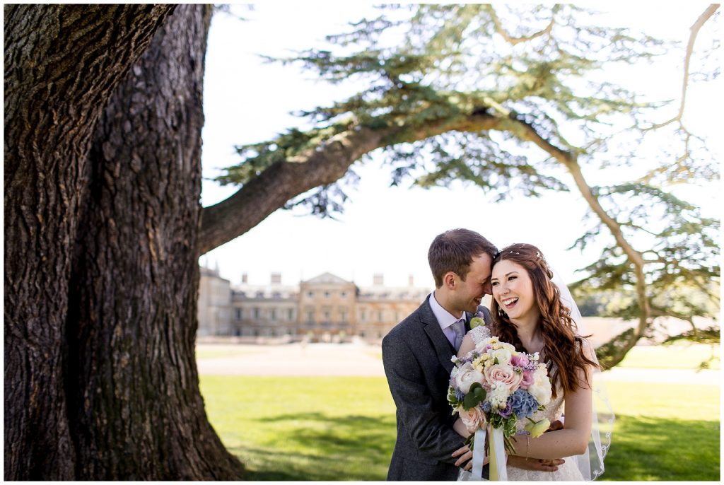 bride and groom laugh together under the tree in front of the woburn abbey