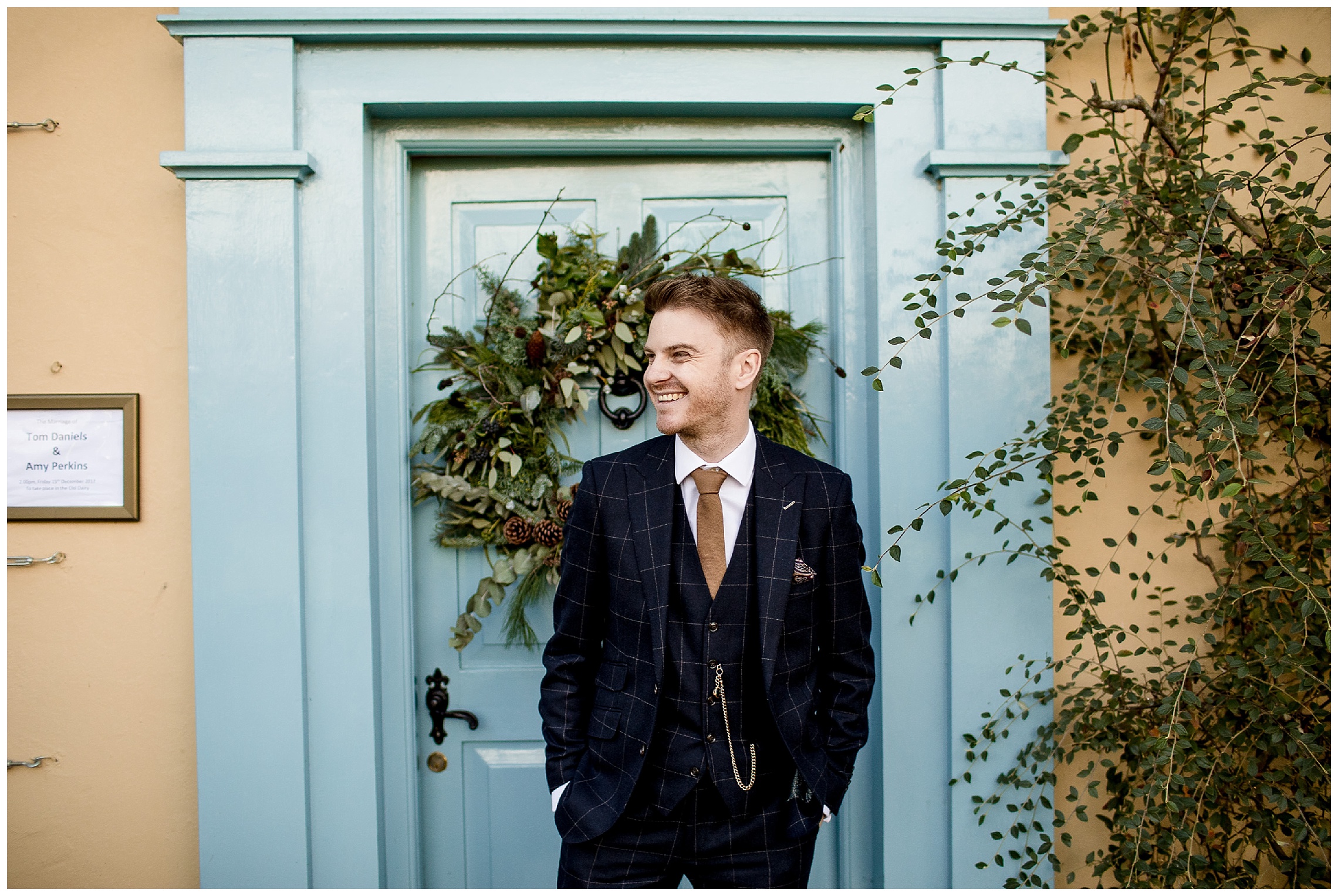 groom stood in front of blue wreathed door at south farm