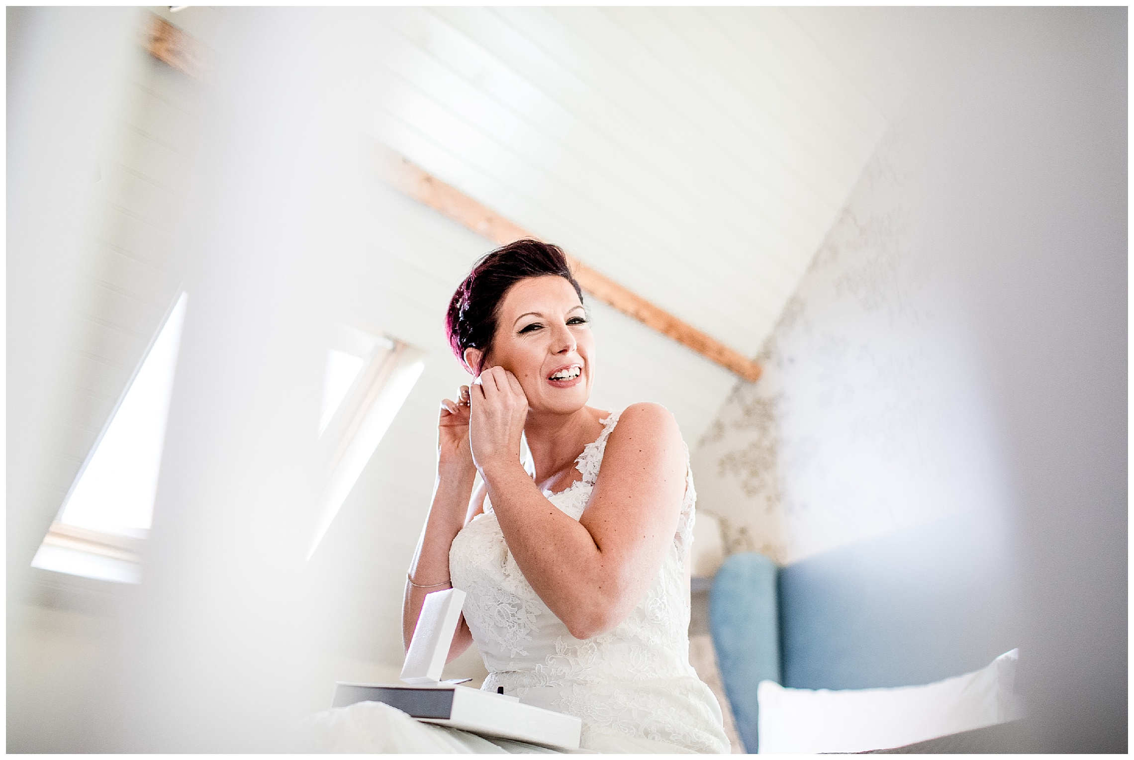 bride sits on the bed and puts her earrings in smiling