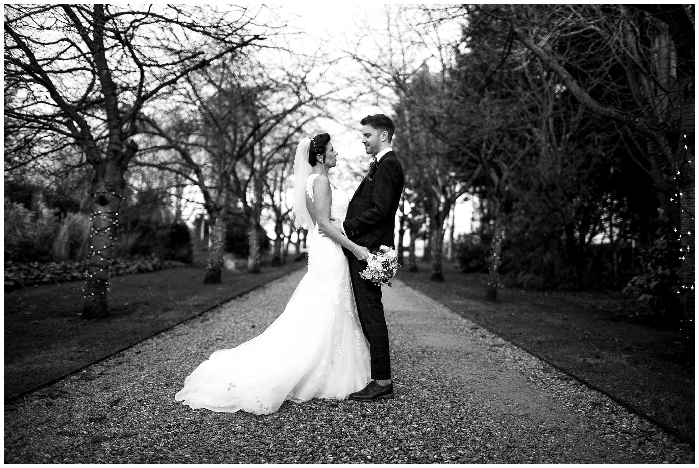 bride and groom stand together in the tree covered driveway at south farm