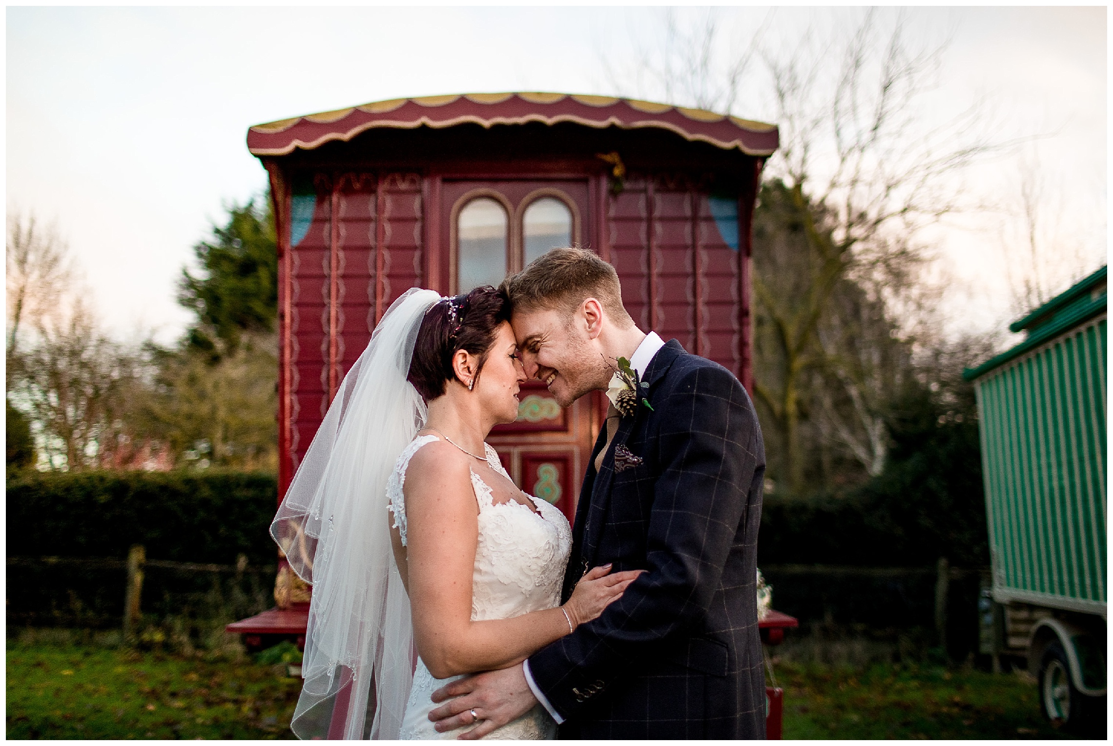 bride and groom with heads together in front of romany caravans