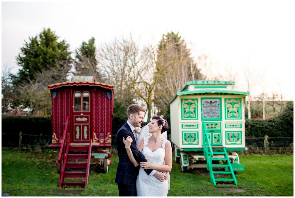 bride and groom embrace in front of the romany caravans at south farm wedding venue