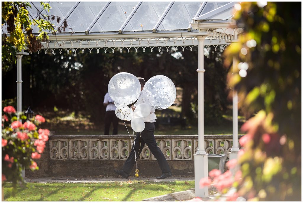 groom walking with balloons into wedding marquee 
