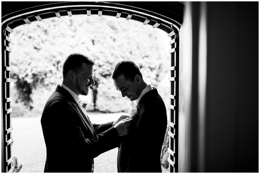 Best man adjusting buttonhole for groom in doorway of house 