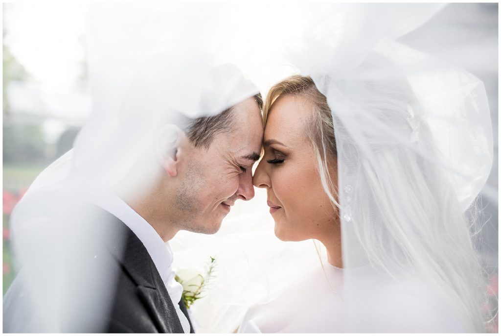 Bride and groom share a tender moment under the veil outside at plum park 