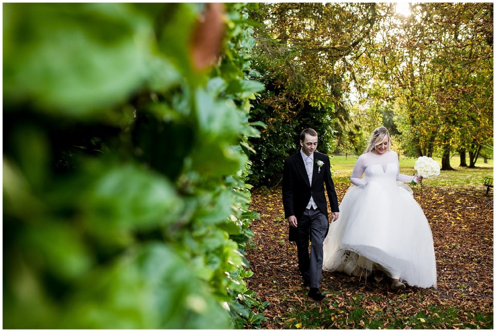 Bride and groom walk together through leaves at autumn 