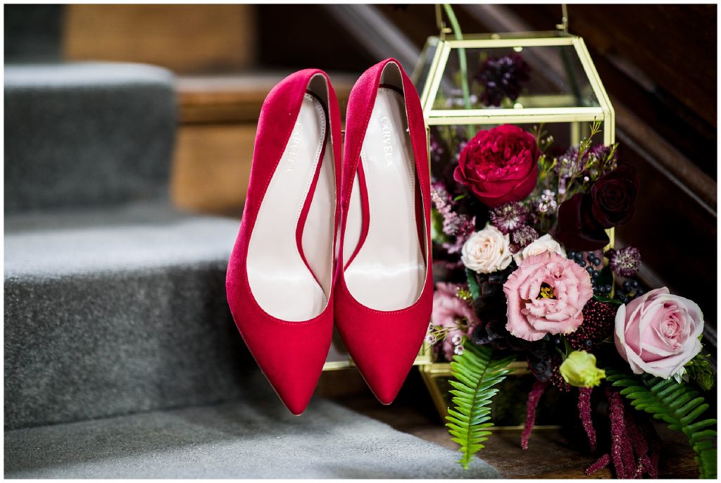 brides red shoes hanging on red and rich coloured floral display 