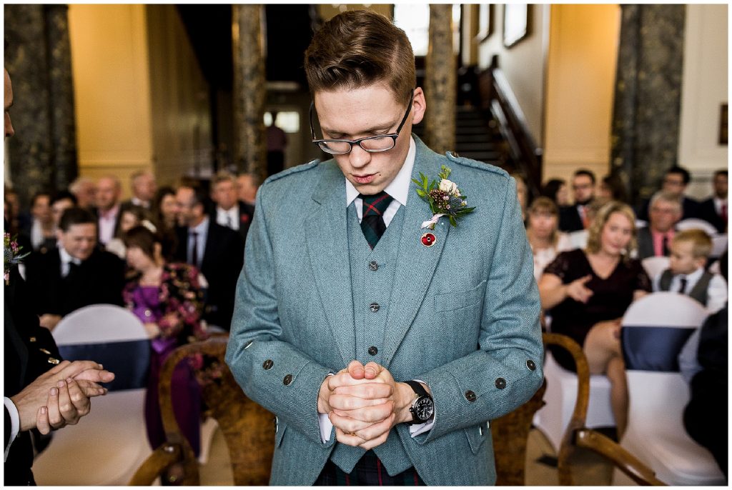 groom stands at end of aisle clasping hands and breathing 