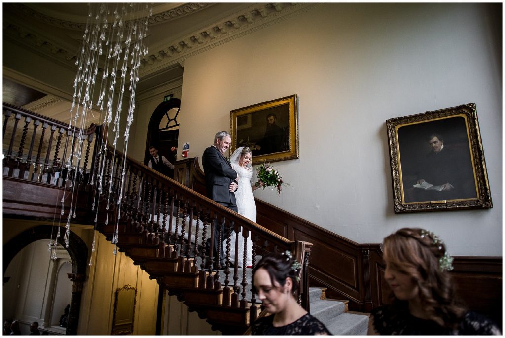 bride and brides father walk down stairs towards aisle 
