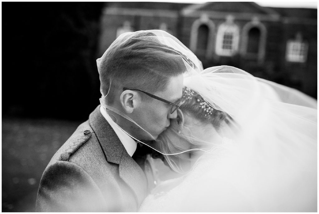 bride and groom embrace under veil in front of wedding venue