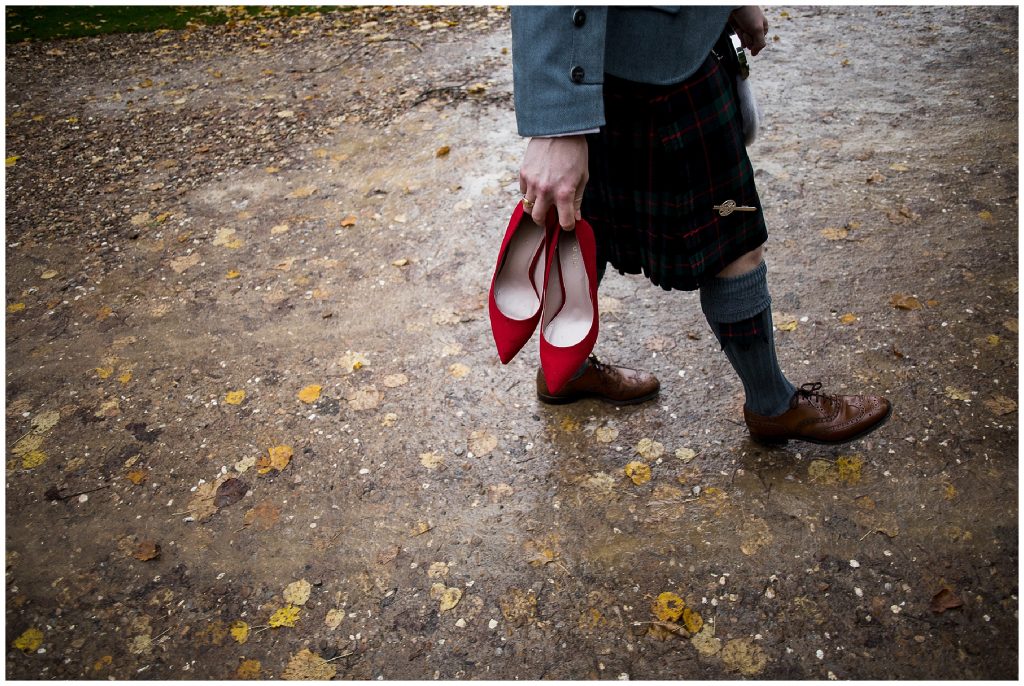groom carries brides red shoes in the rain