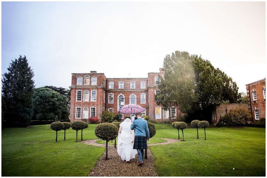 bride and groom walk through rain under poppy umbrella