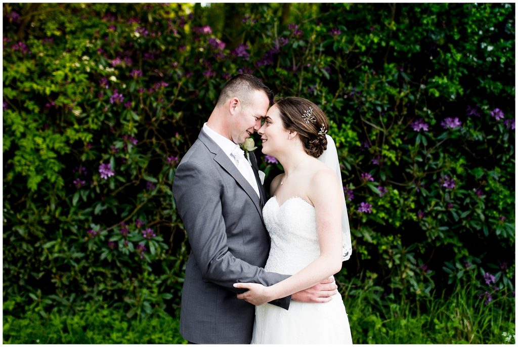 bride and groom embrace in front of a floral bush