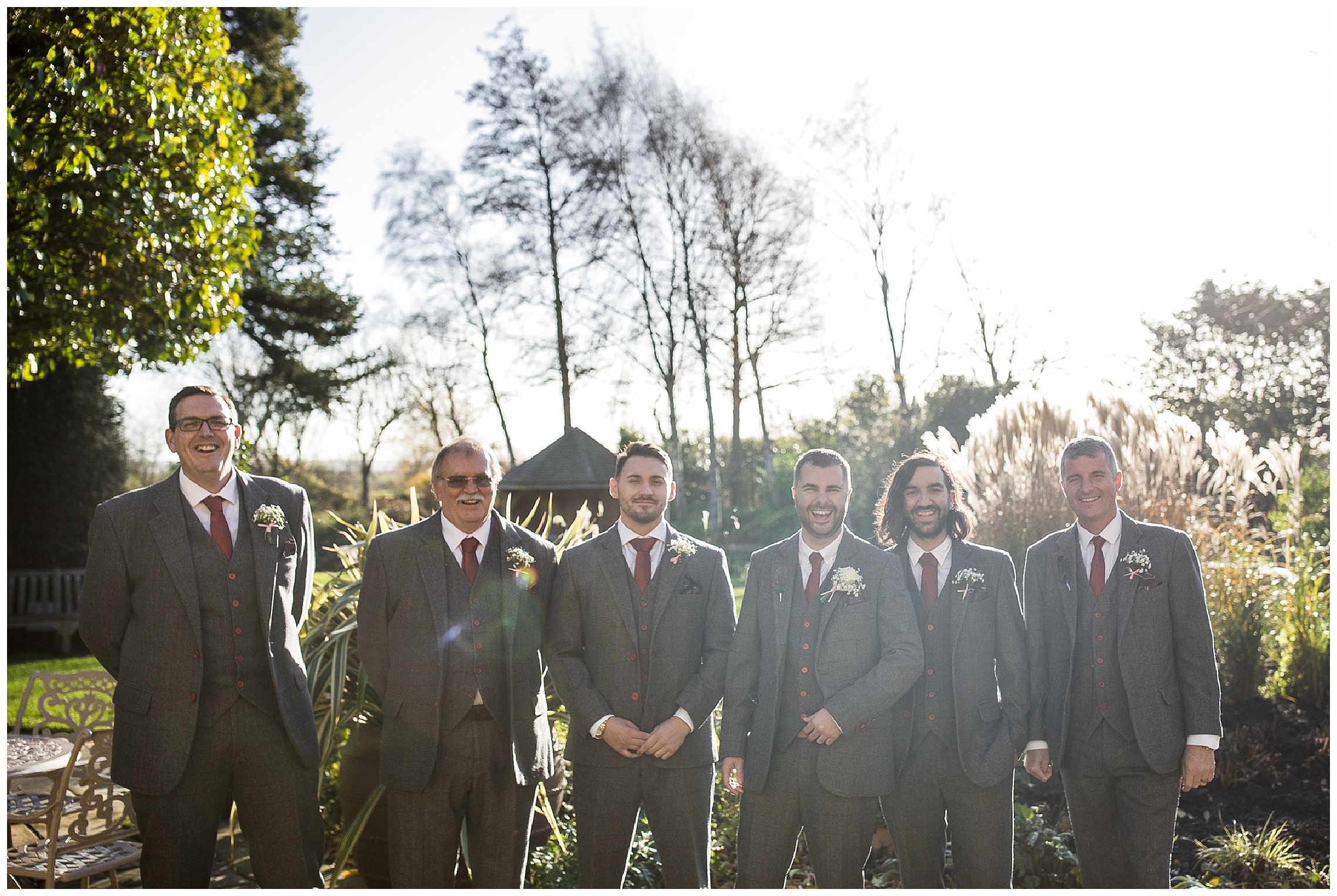 groomsmen standing outside in sun together smiling before ceremony