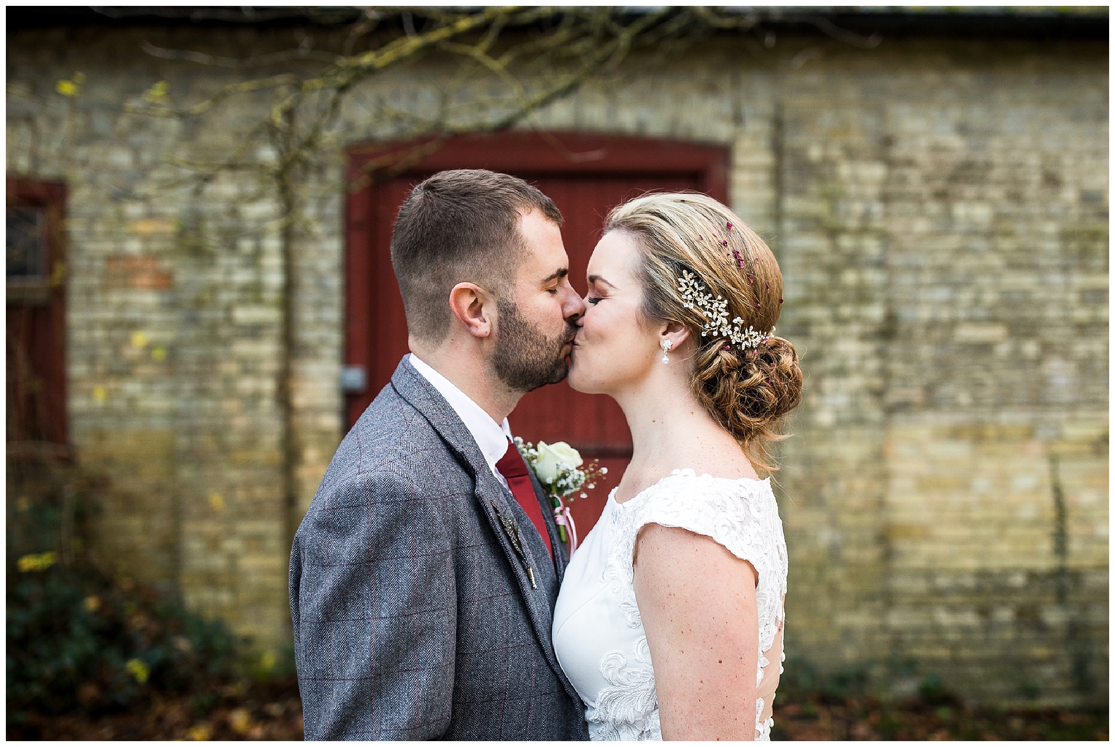 Bride and groom kiss in front of brick wall with red door