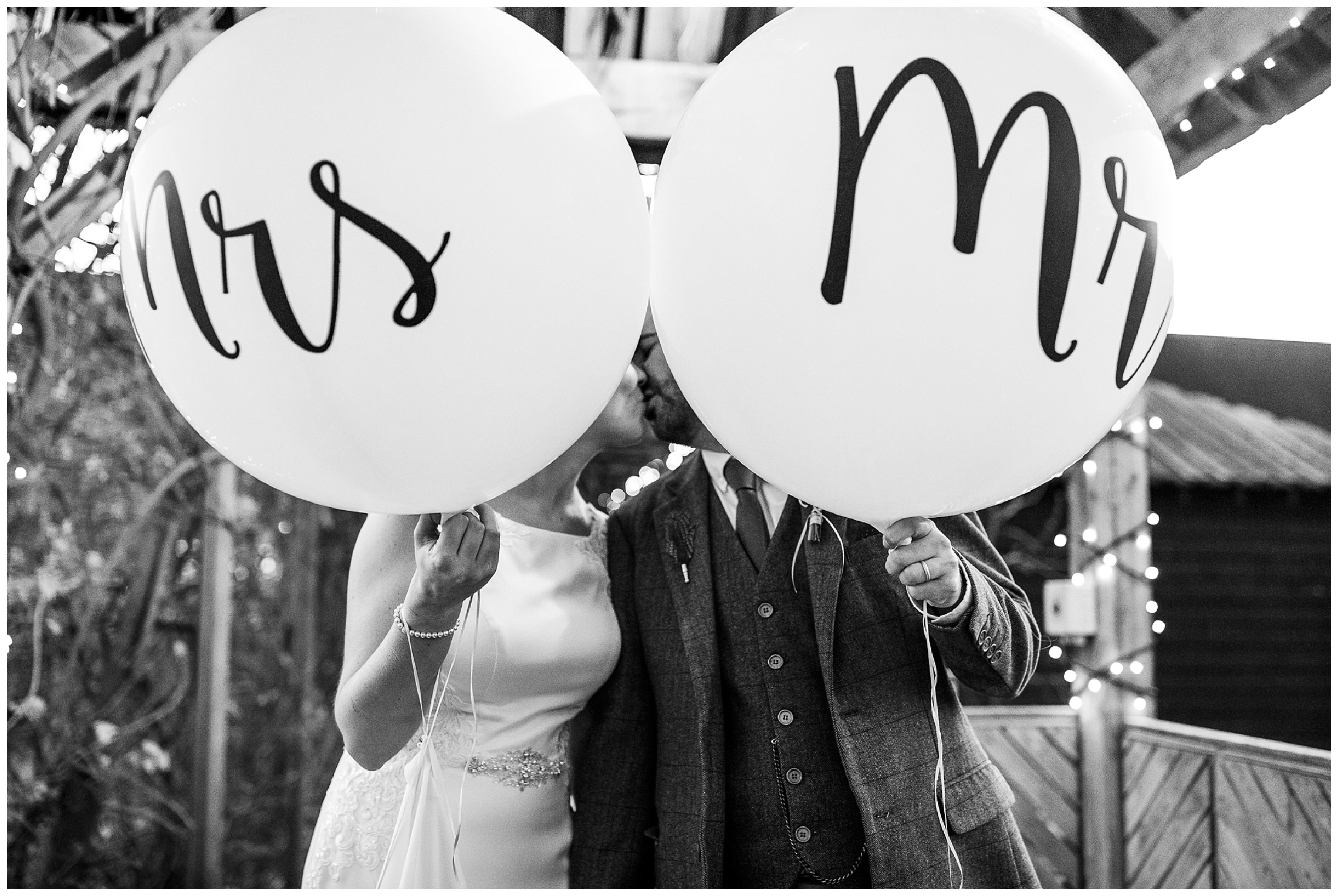 bride and groom kiss behind mr and mrs balloons