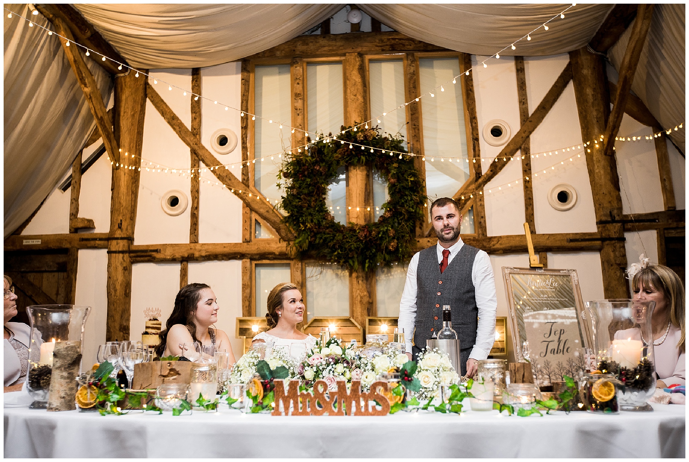 Groom gives speech from top table in barn venue