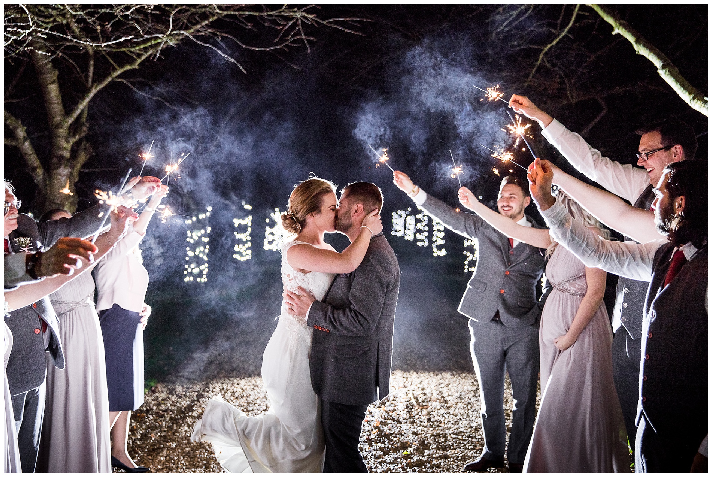 sparklers outside with bridesmaids and groomsmen, bride and groom kissing