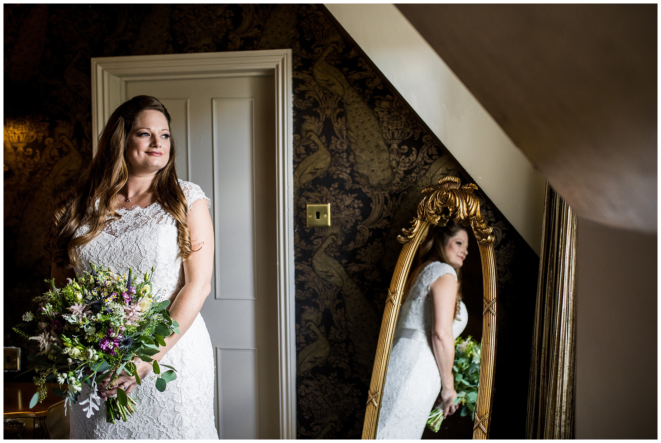 bride in her wedding dress holds onto her bouquet of greenery looking out of the window