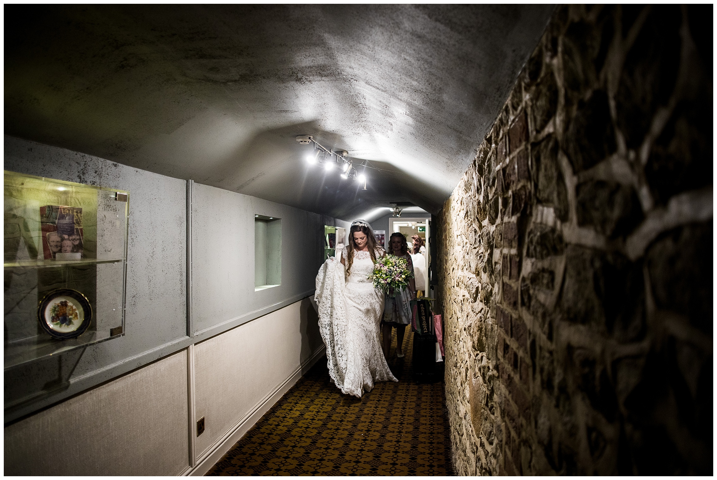 bride walks down dark corridor holding her dress off the floor