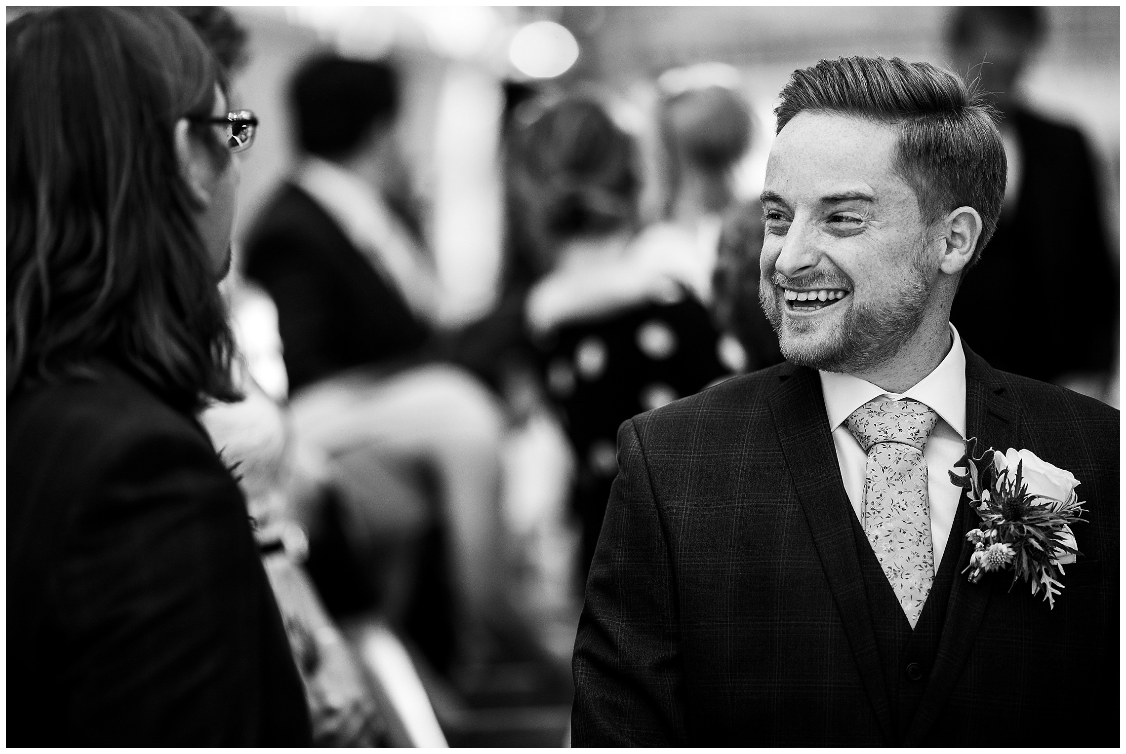 black and white image of groom smiling as bride approaches