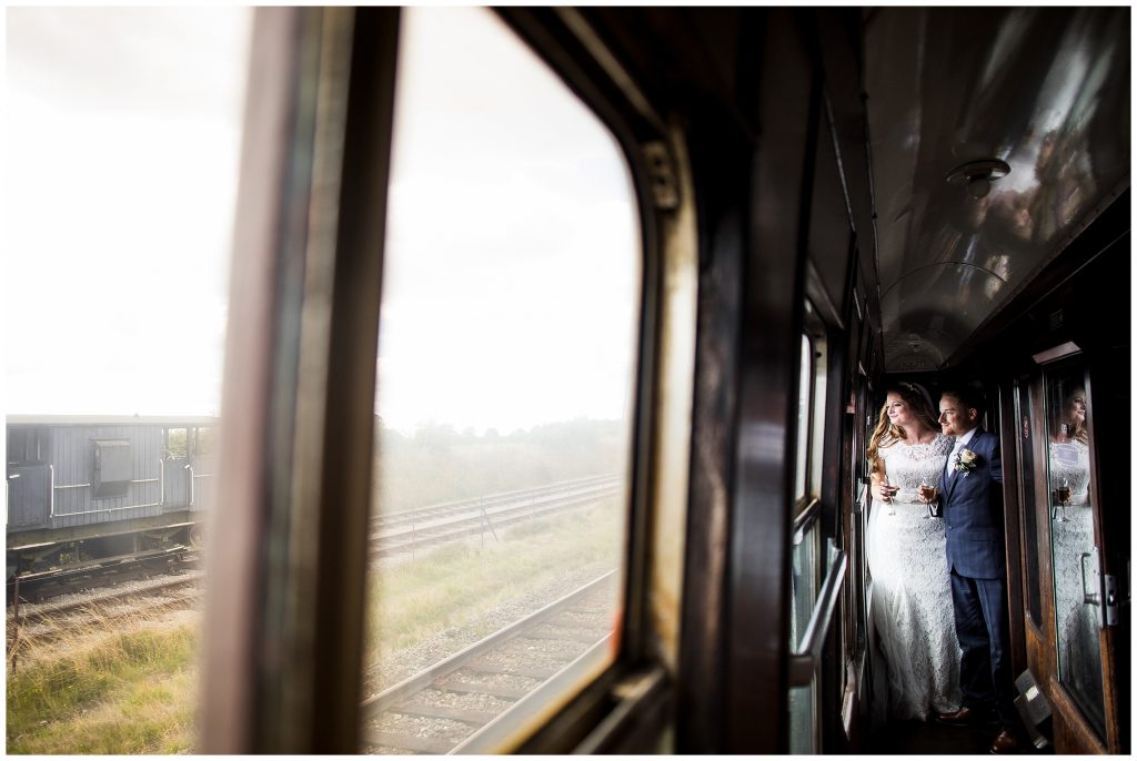 bride and groom stand close together and look out of window of steam train