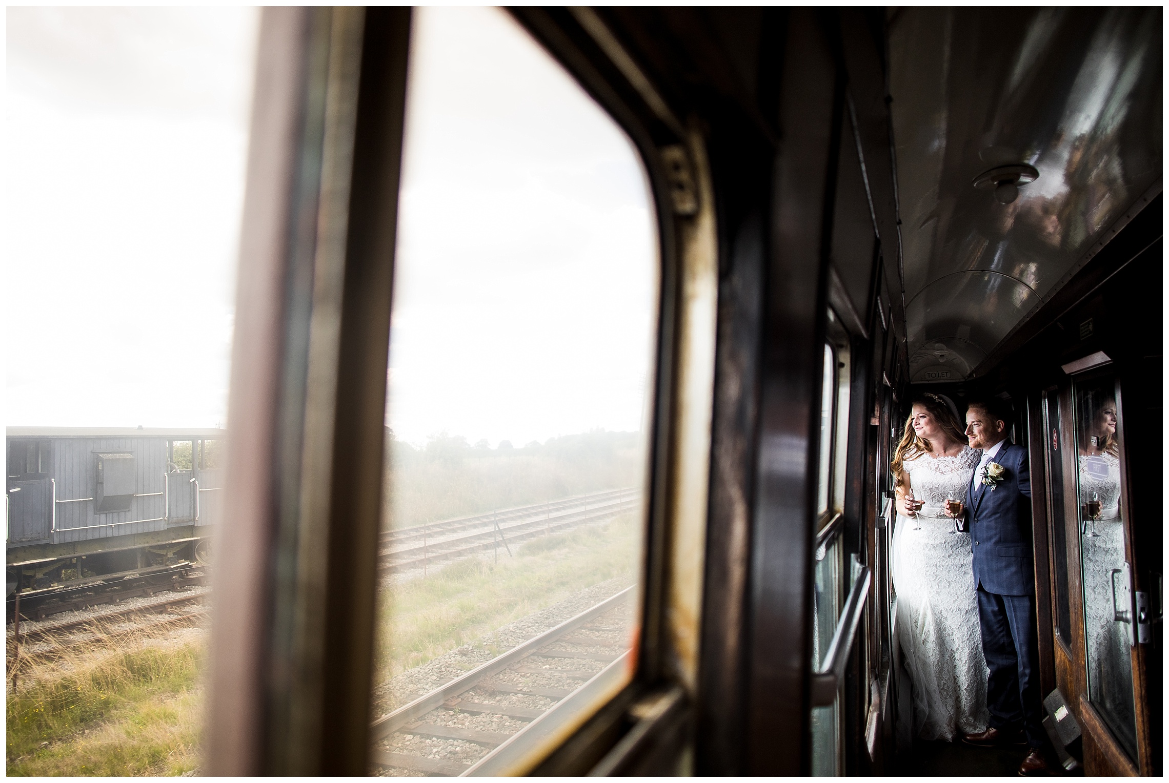 bride and groom stand close together and look out of window of steam train