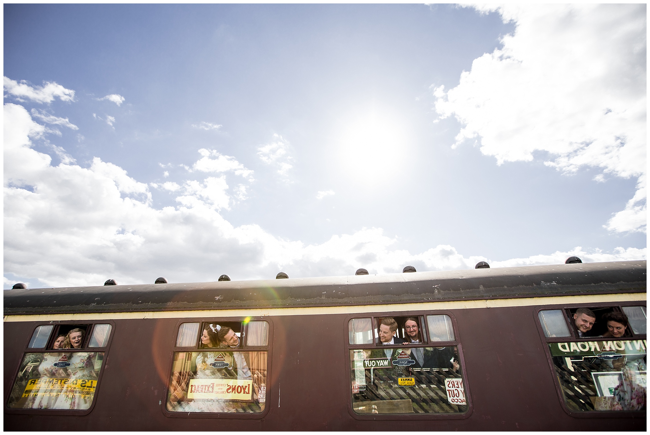 Groomsmen and bridesmaids hanging out of vintage steam train windows laughing at bucks railway centre
