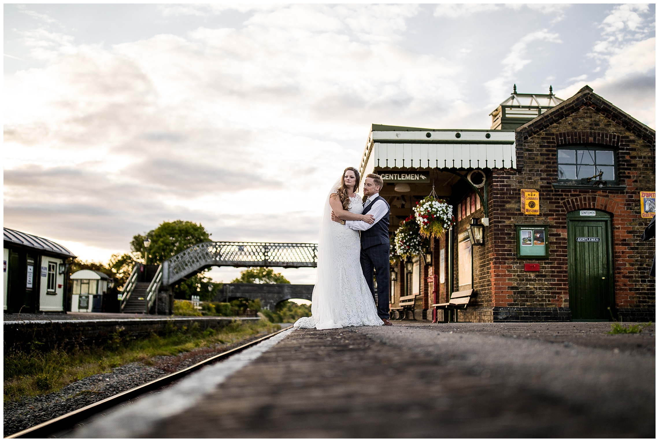 bride and groom stand at edge of old train platform, arm in arm as the sun goes down over bucks railway centre