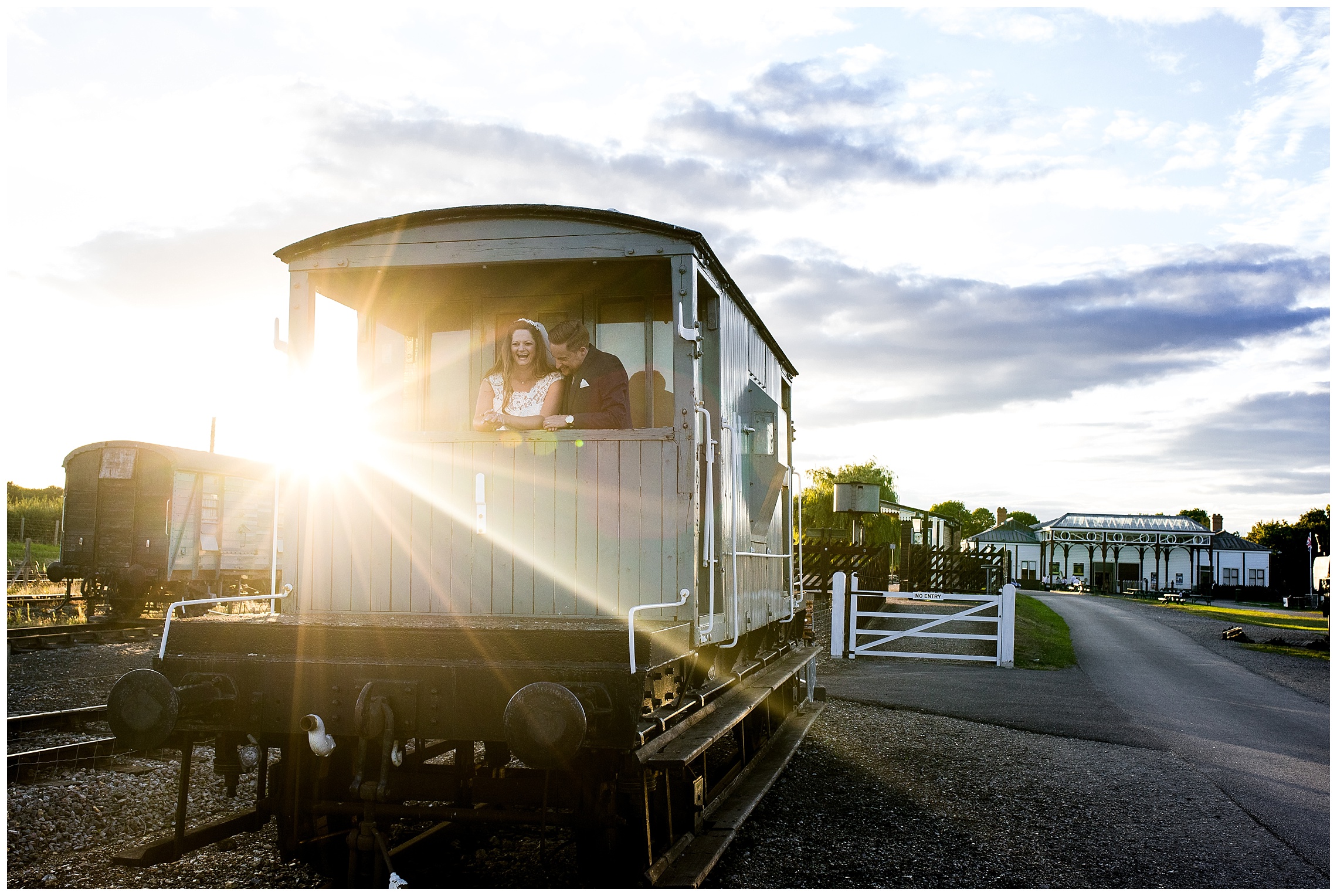 bride and groom stood in train trailer laughing as the sun sets