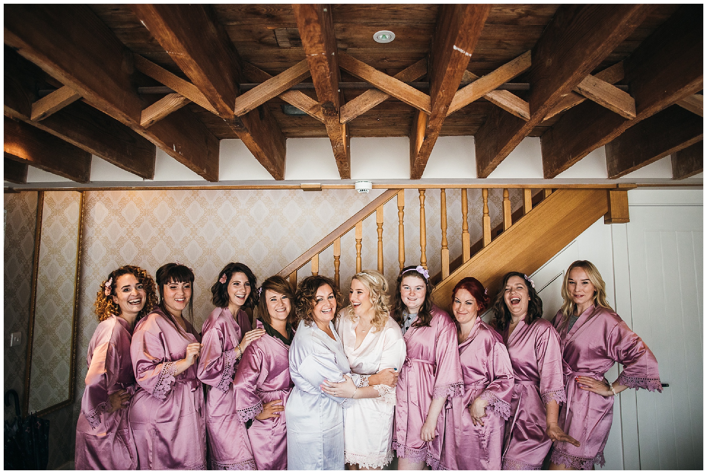Bride and bridesmaids squeeze together smiling in dressing gowns at bassmead