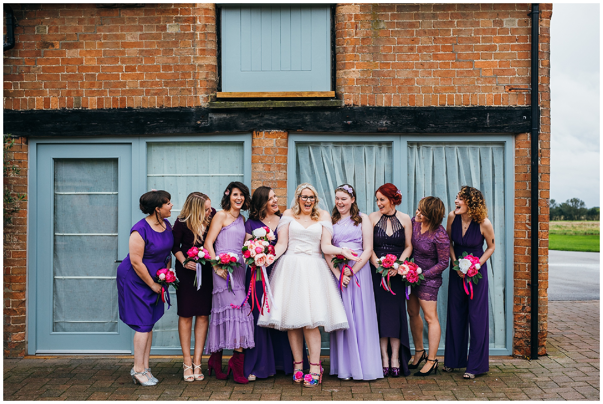 Bride in Mooshki dress and bridesmaids in different shades of purple dresses with pink flowers