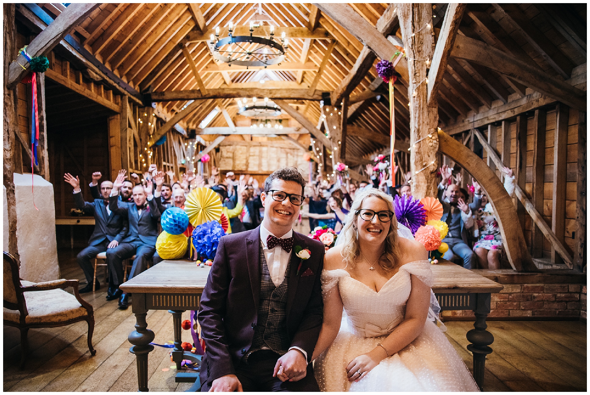 bride and groom sit together surrounded by their guests and colourful decorations