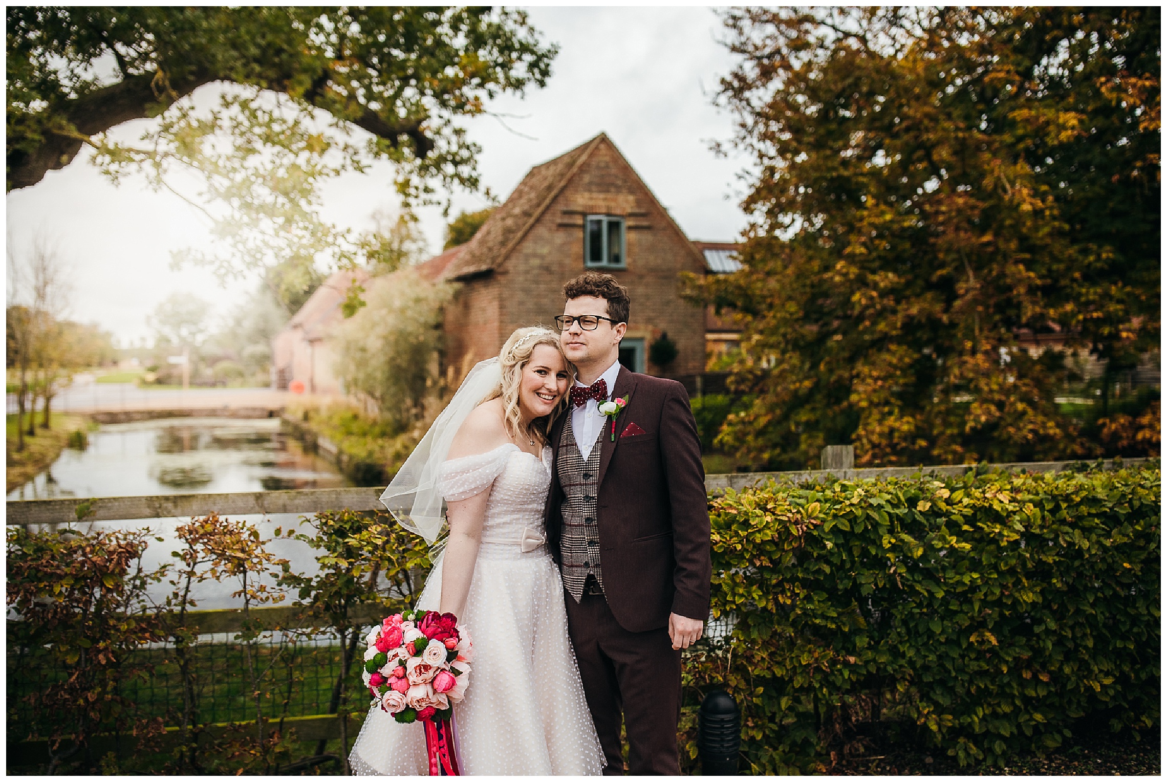 bride and groom cuddle in front of water at bassmead manor