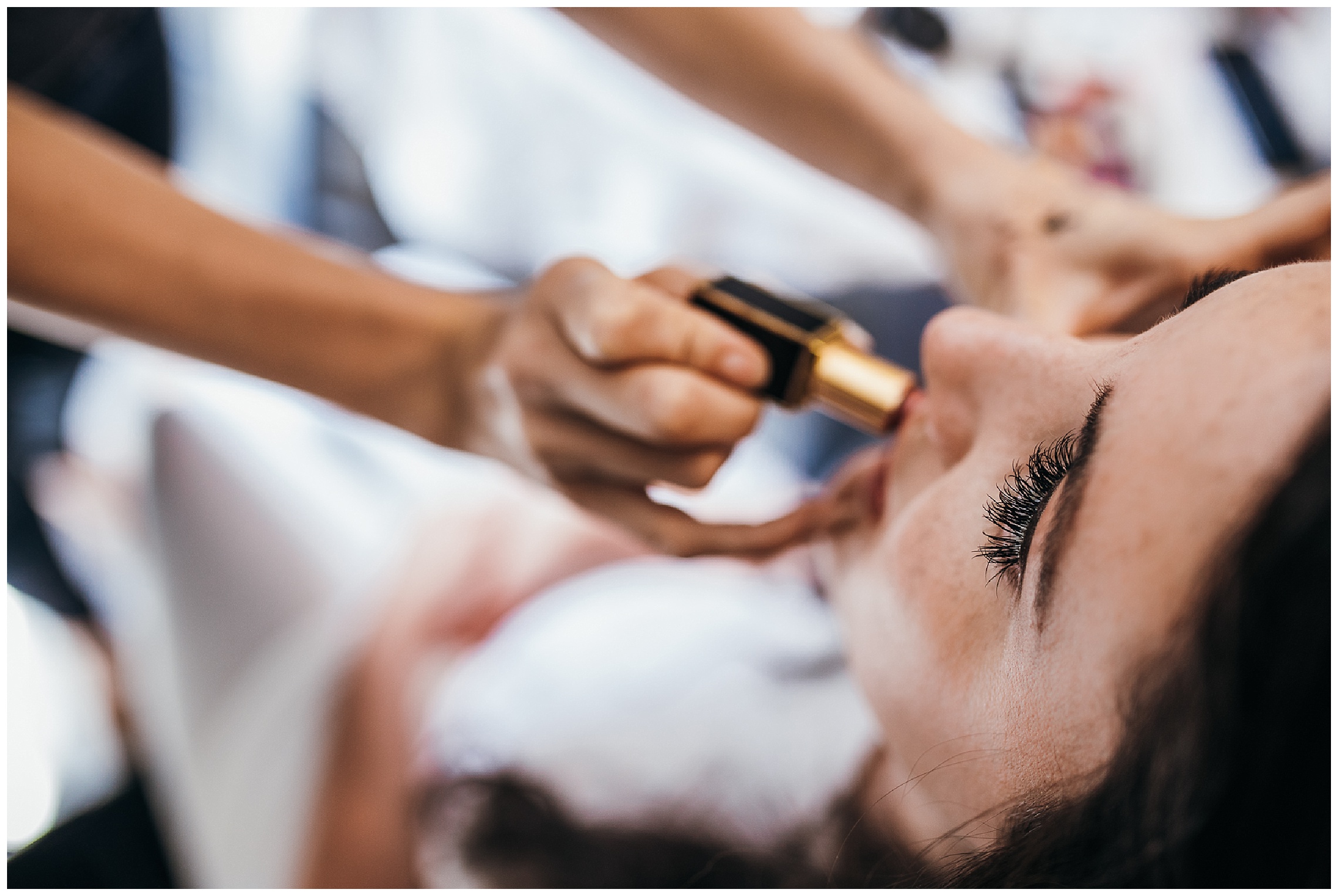 Make up artists applies red lipstick to bride with dark hair and long eyelashes