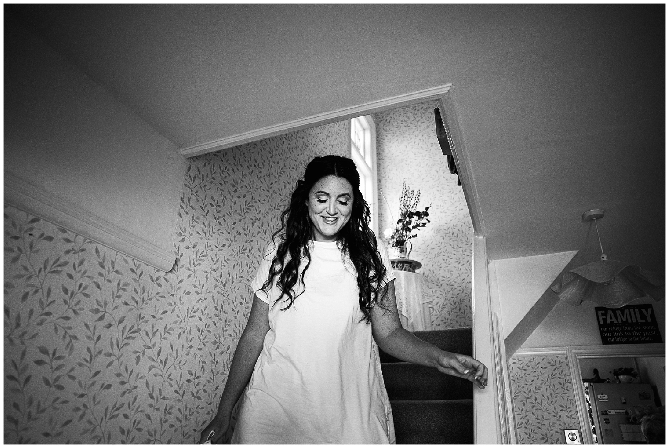 black and white image of bride smiling as she walks down the stairs in a t-shirt