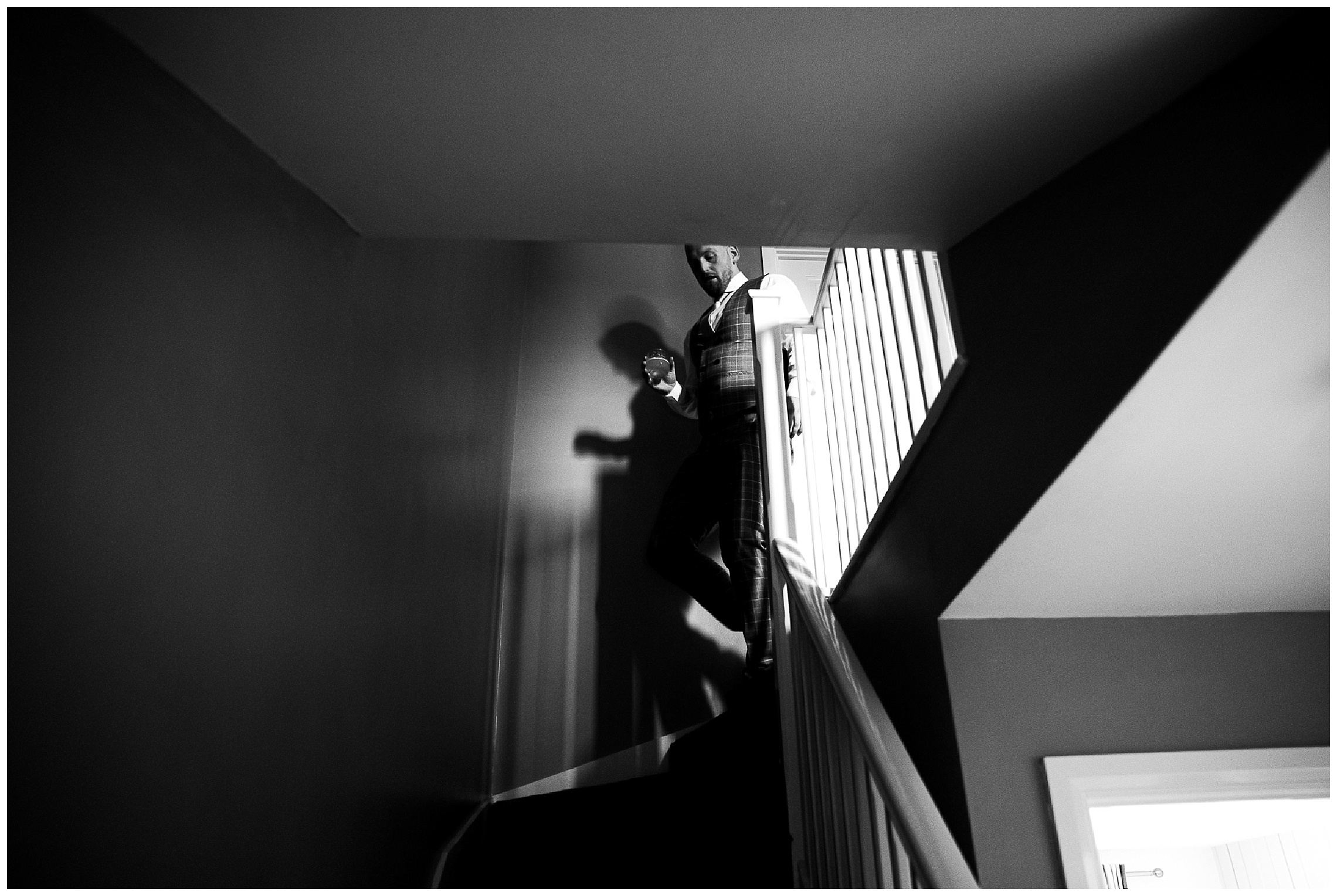 black and white image of groom in suit walking down stairs at home