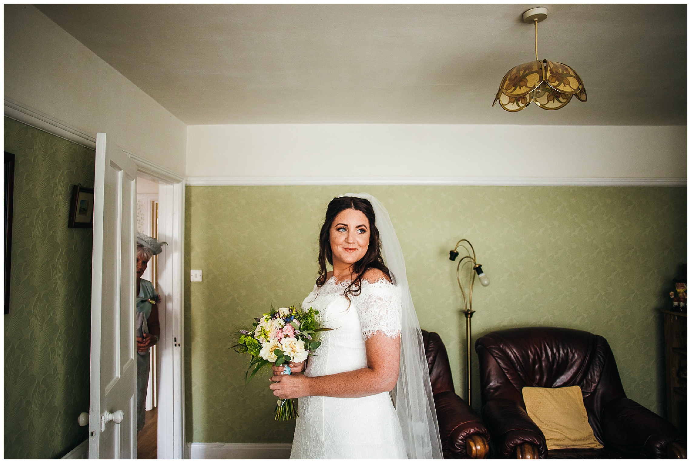 Bride looks over shoulder in wedding dress as mum looks on and smiles