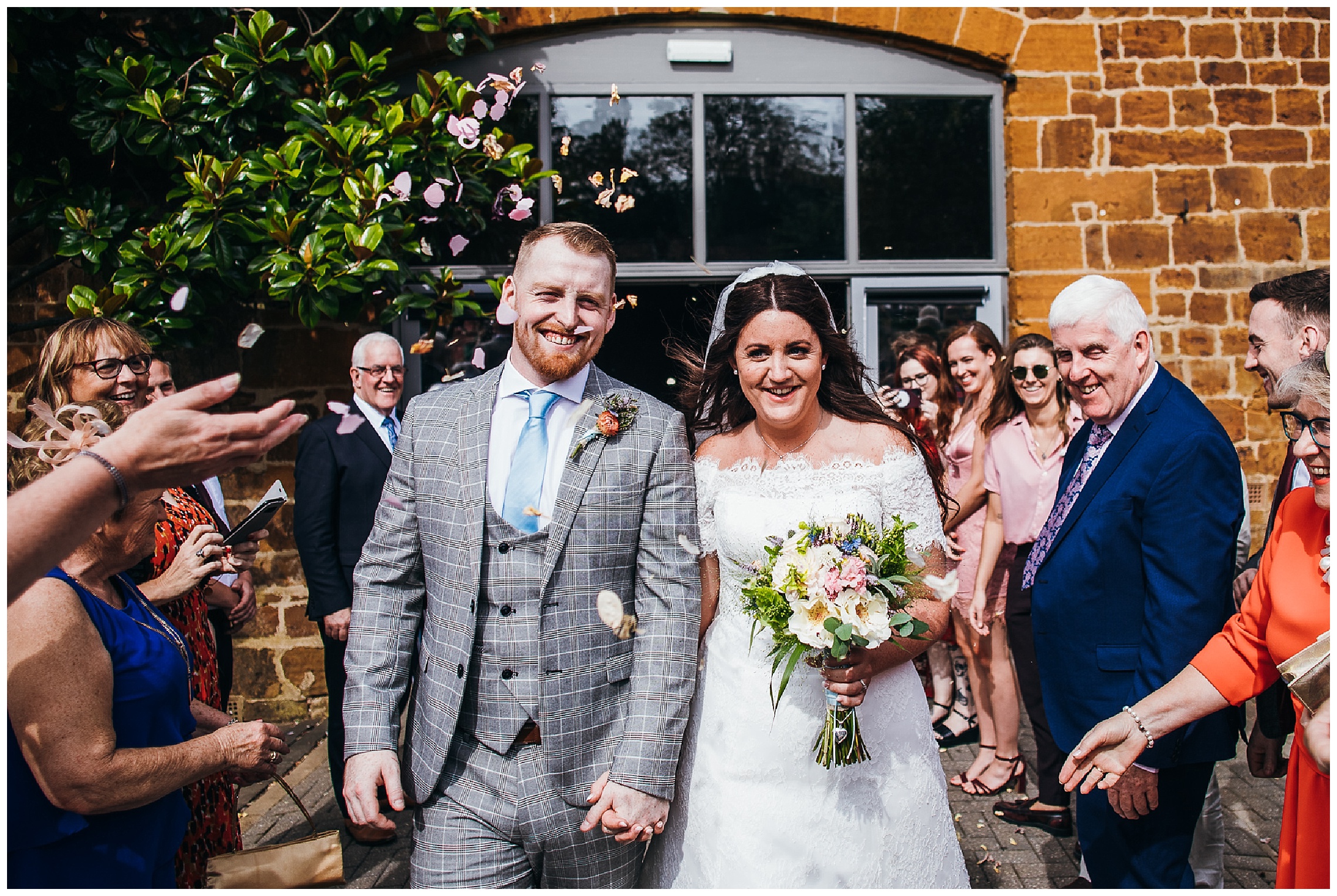 bride and groom walk underneath natural confetti surrounded by smiling wedding guests at hunsbury hill