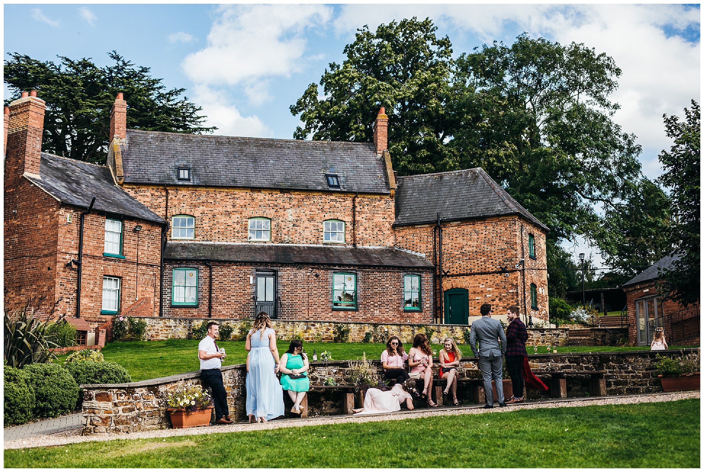guests stand outside with blue sky and green grass at brick wedding venue
