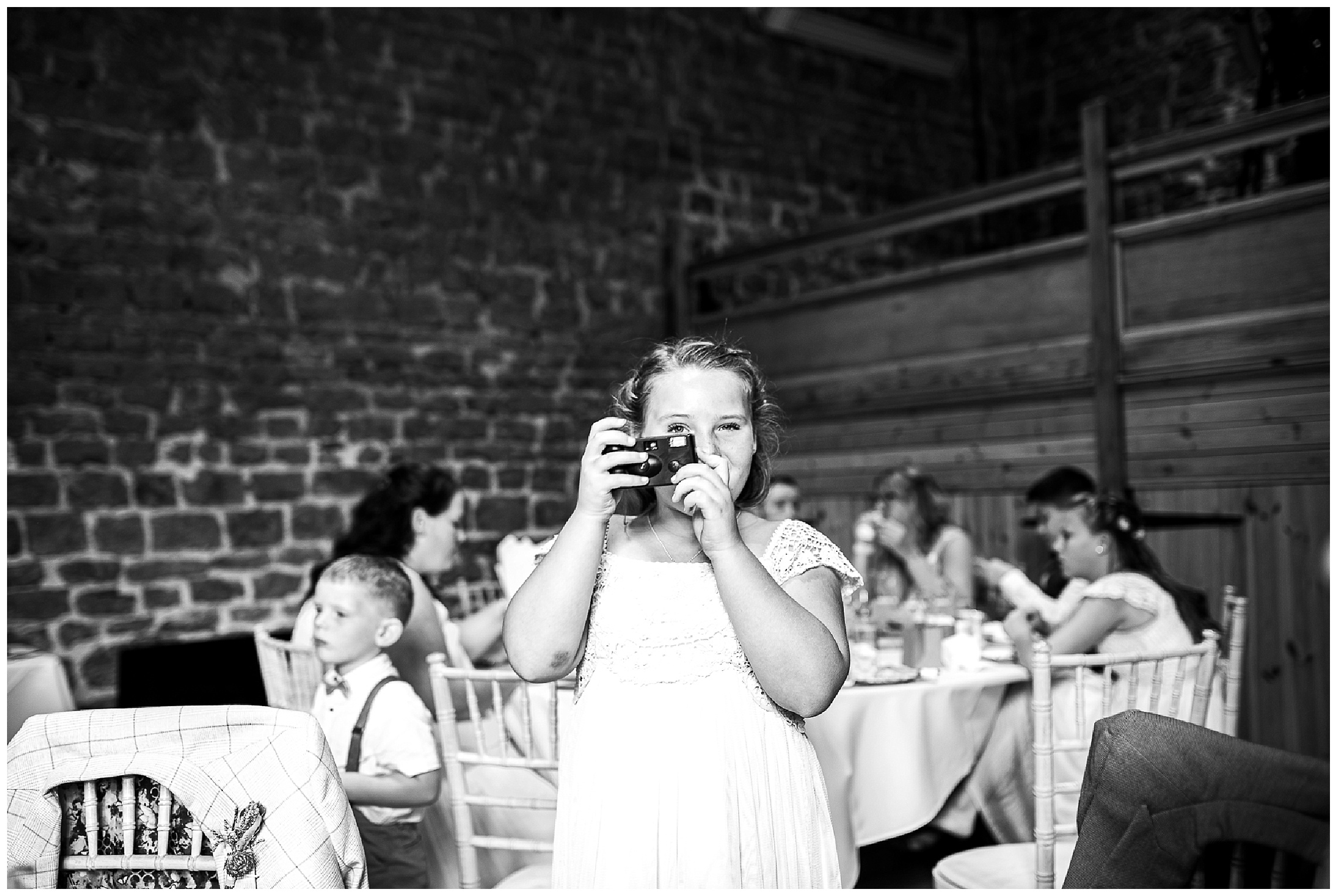 black and white image of little flower girl taking photo on disposable camera