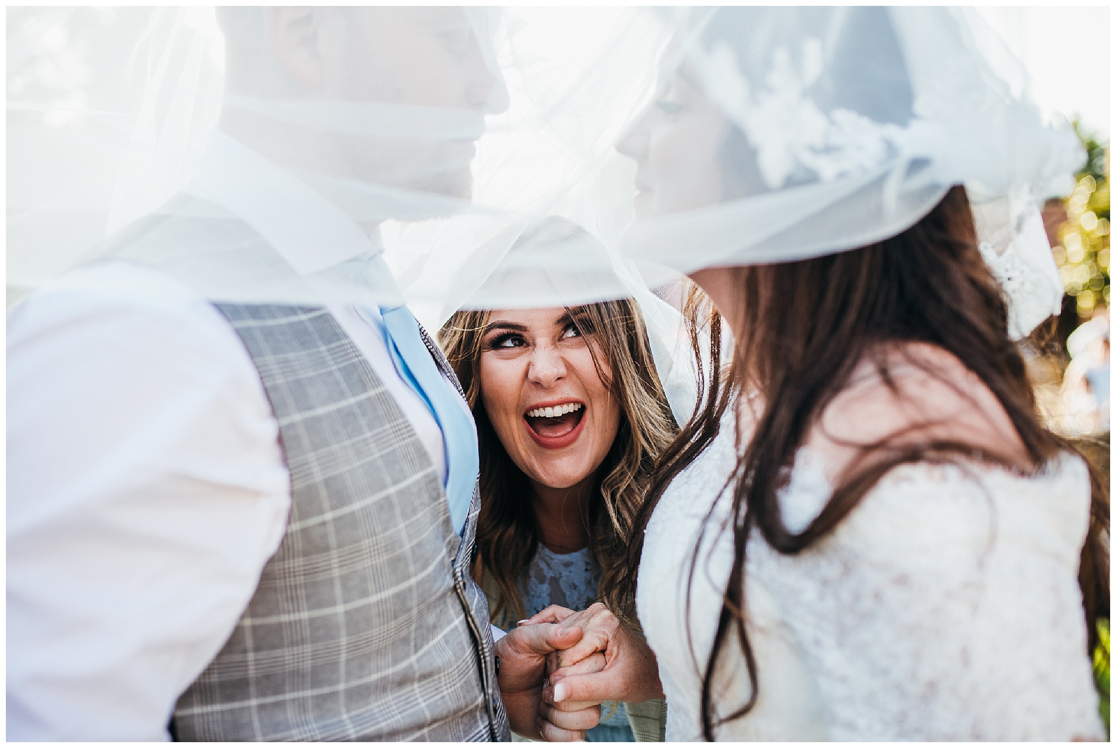 bridesmaid interrupts bride and groom kissing and pops under veil laughing