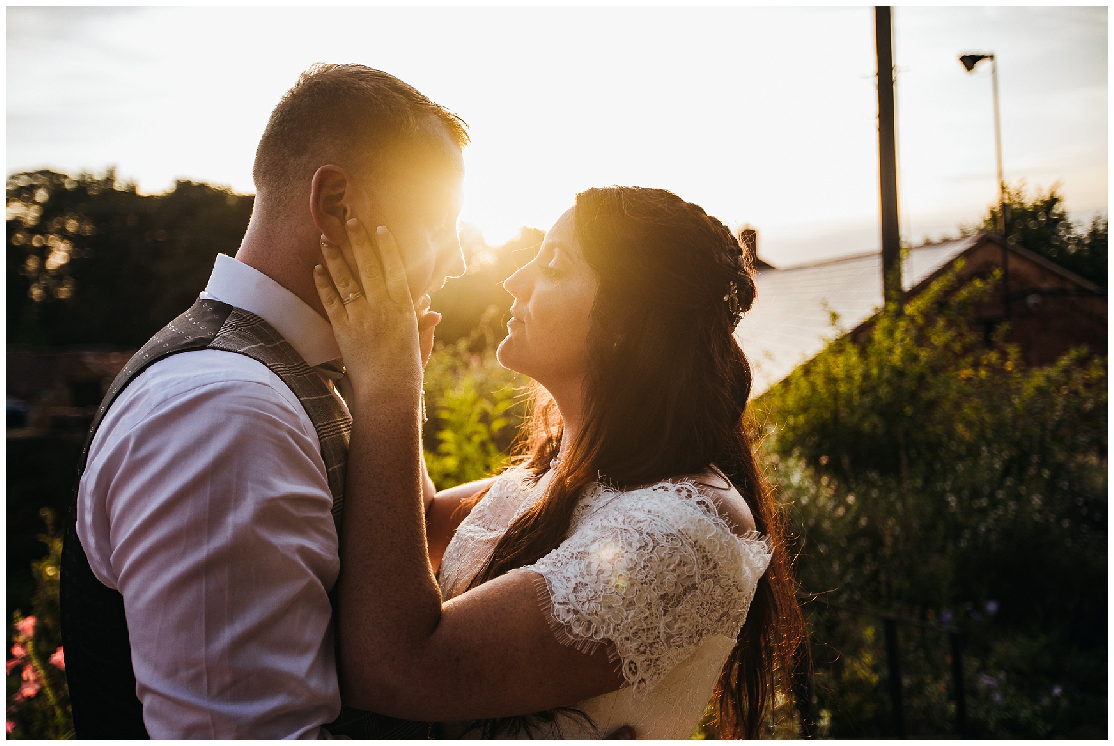 bride pulls groom in by the face for a kiss in front of sun setting