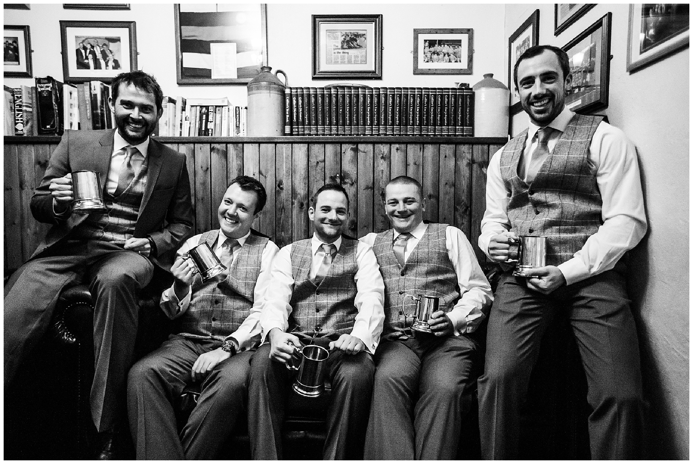 groom and groomsmen sitting in wooden pew in pub drinking beer