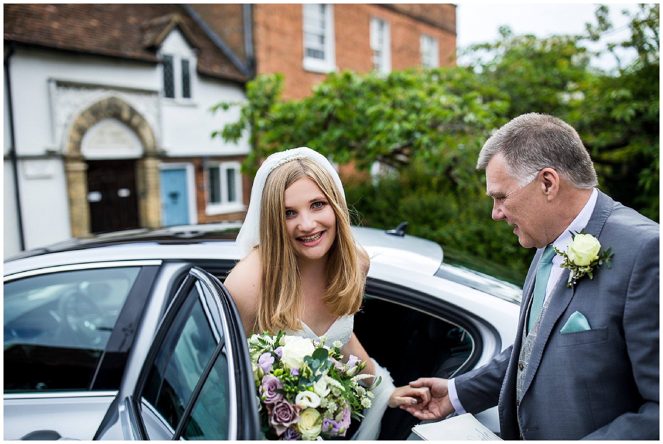 Bride getting out of silver wedding car with dad holding her hand