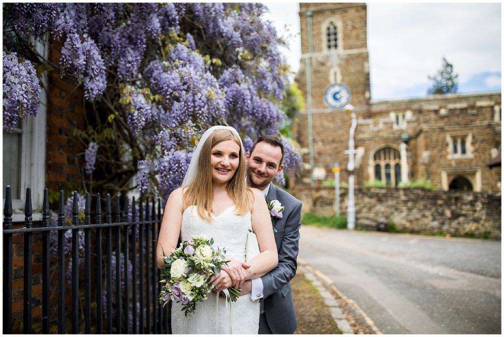 bride and groom stood next to wisteria in front of ampthill church