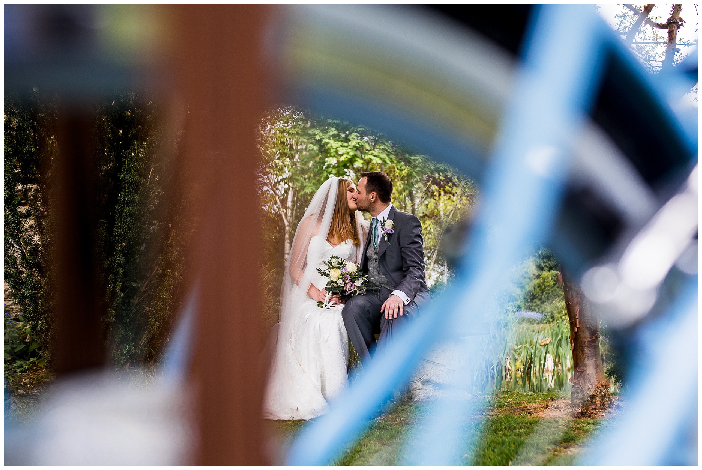 Bride and groom kiss privately surrounded by greenery and blue bike