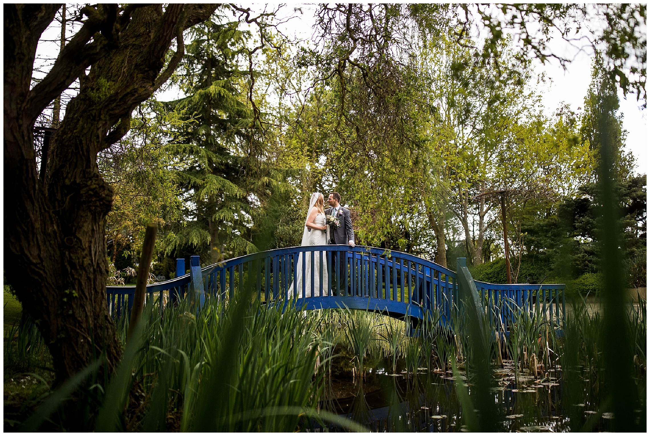 Bride and groom stand on bridge over lake at Flaxbourne Gardens Weddings