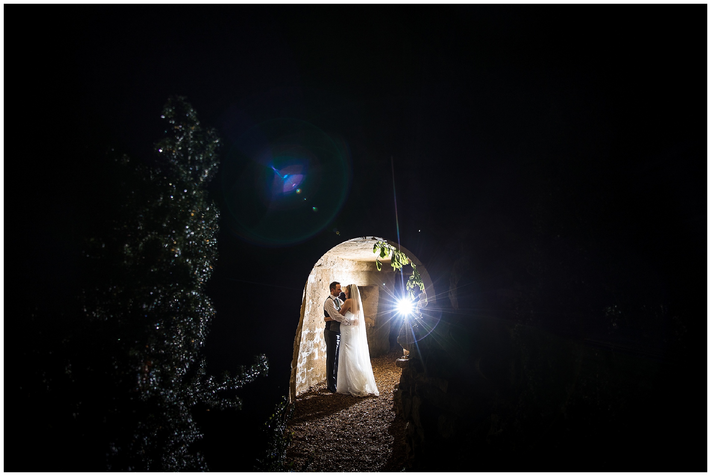 Bride and groom stood next to waterfall in dark, illuminated by spotlight