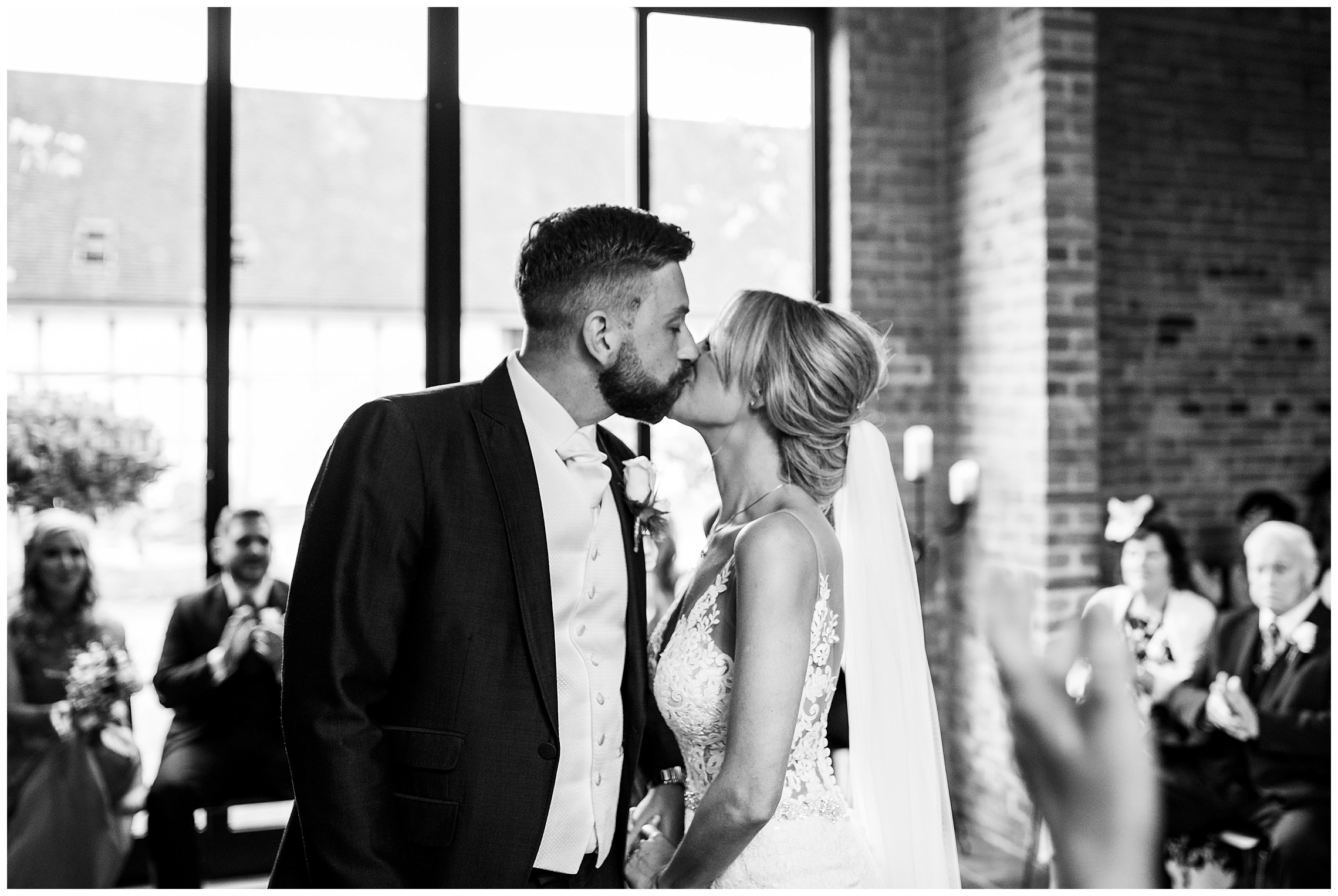 bride and groom kissing during wedding ceremony in front of windows